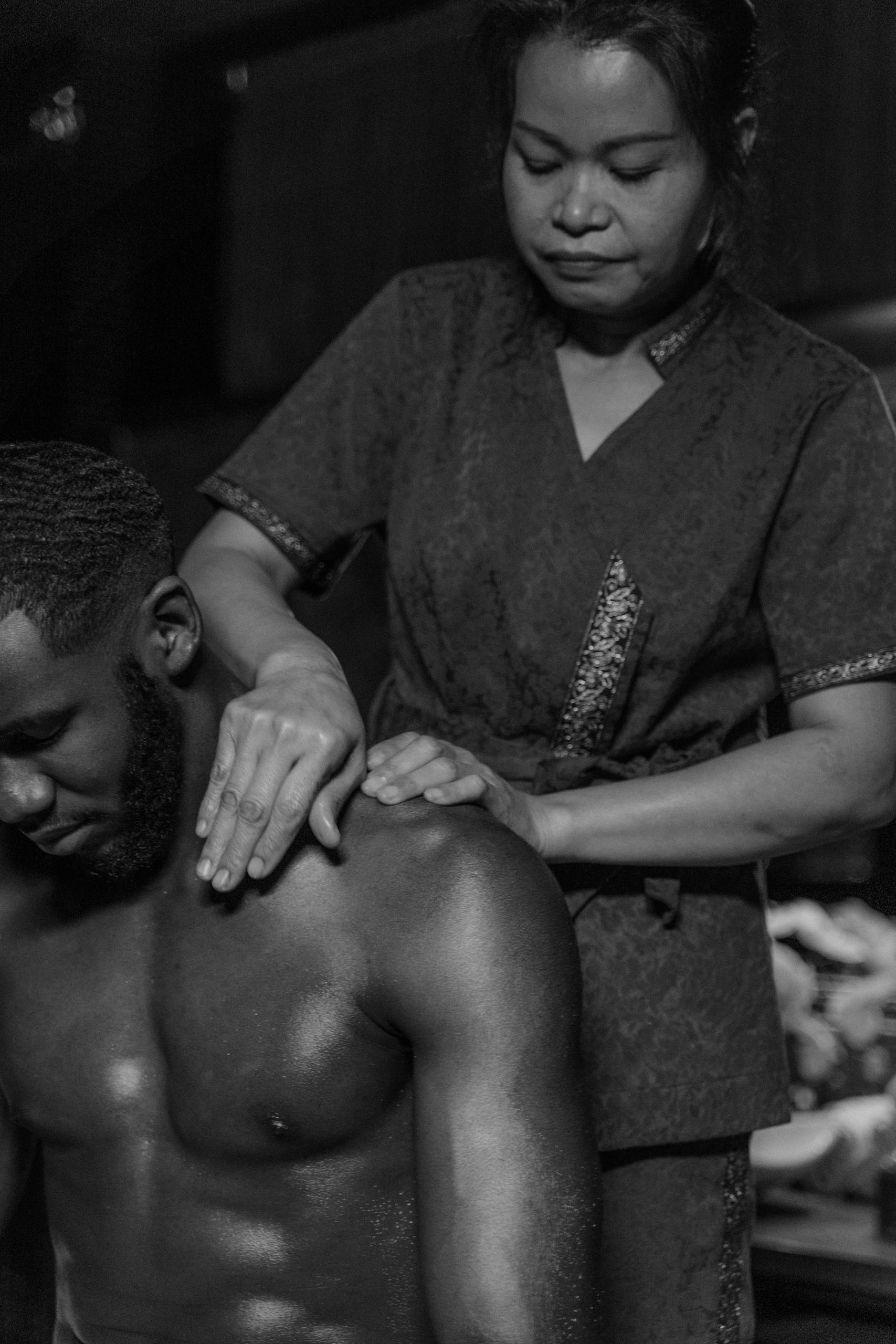 Black and white photo of a massage therapist working on a man's shoulders, conveying relaxation and tranquility.